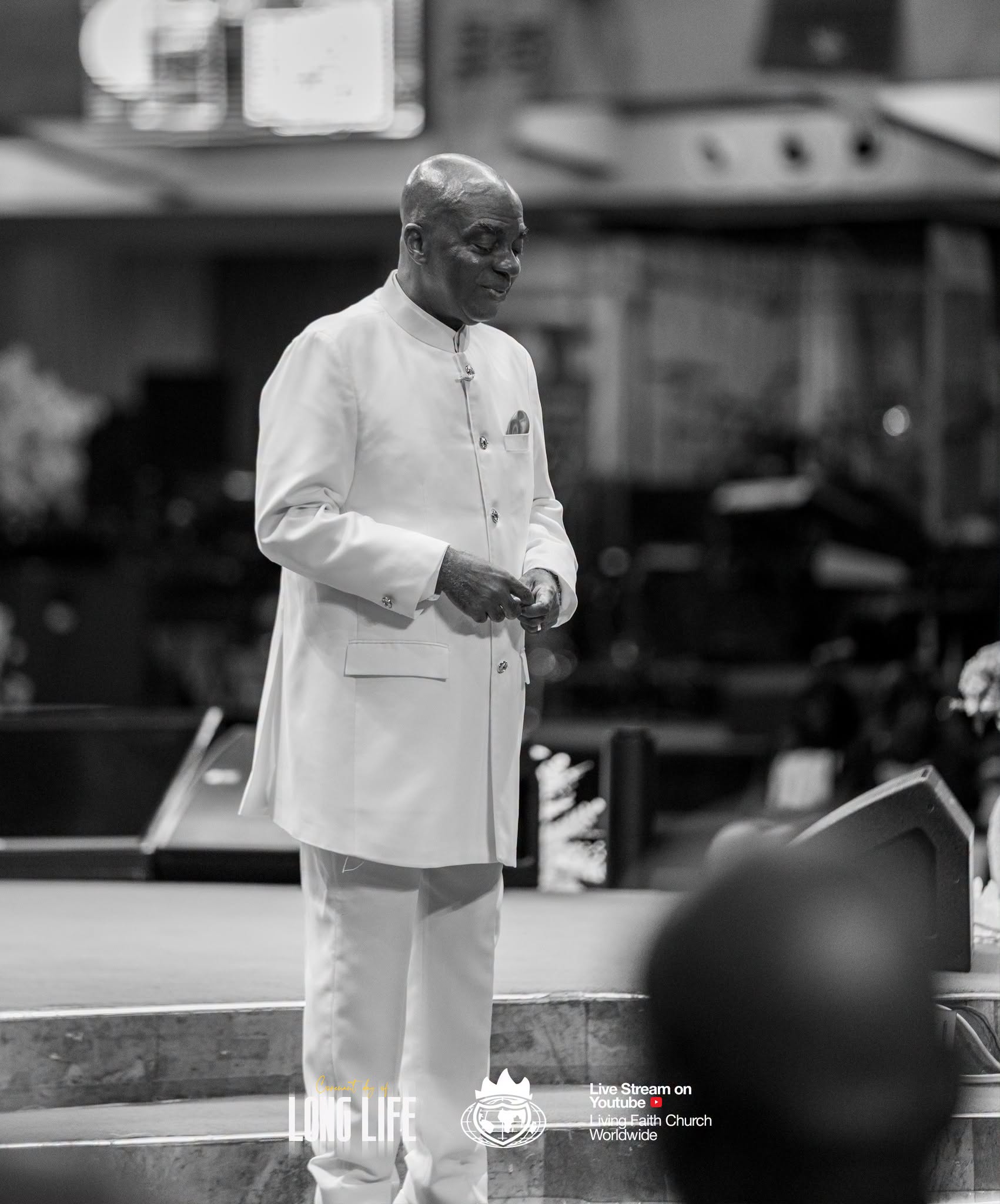 Bishop David Oyedepo standing with hands together, in black and white