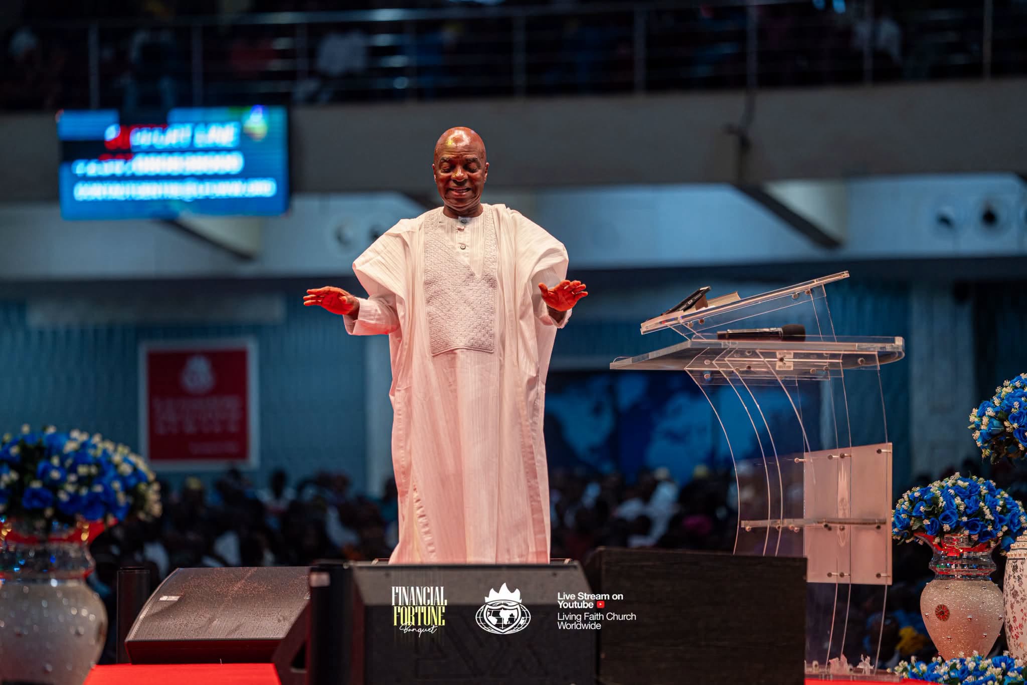 Bishop David Oyedepo in a white agbada on the stage at Faith Tabernacle